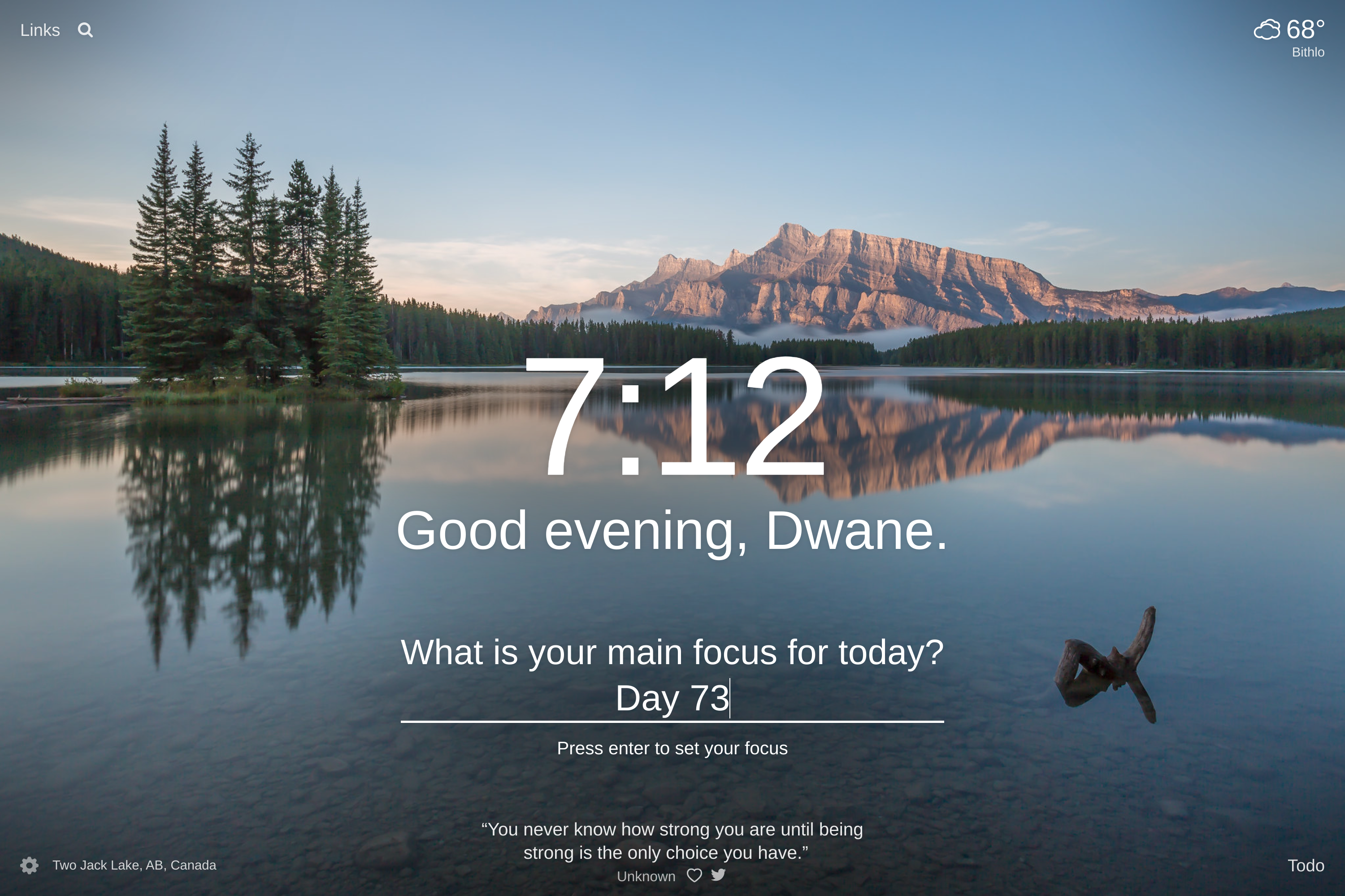 A lake surrounded by a pine tree forest with a mountain in the background and a small island with a few pine trees in the foreground to the left side in Two Jack Lake, AB, Canada